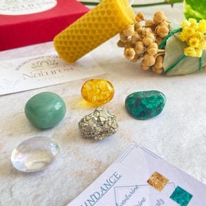 May include: A set of crystals for abundance, including aventurine, citrine, clear quartz, malachite, and pyrite. The set also includes a beeswax candle and a smudge stick.