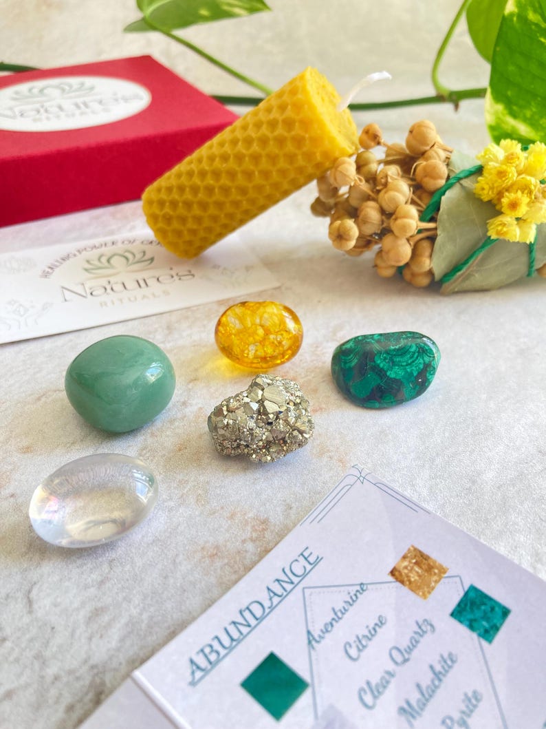 May include: A set of crystals for abundance, including aventurine, citrine, clear quartz, malachite, and pyrite. The set also includes a beeswax candle and a smudge stick.