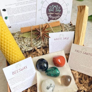 May include: A gift box set for Scorpio zodiac sign with crystals, a beeswax candle, white sage, palo santo, and a cinnamon stick. The box includes a card with the Scorpio zodiac symbol and information about the crystals.