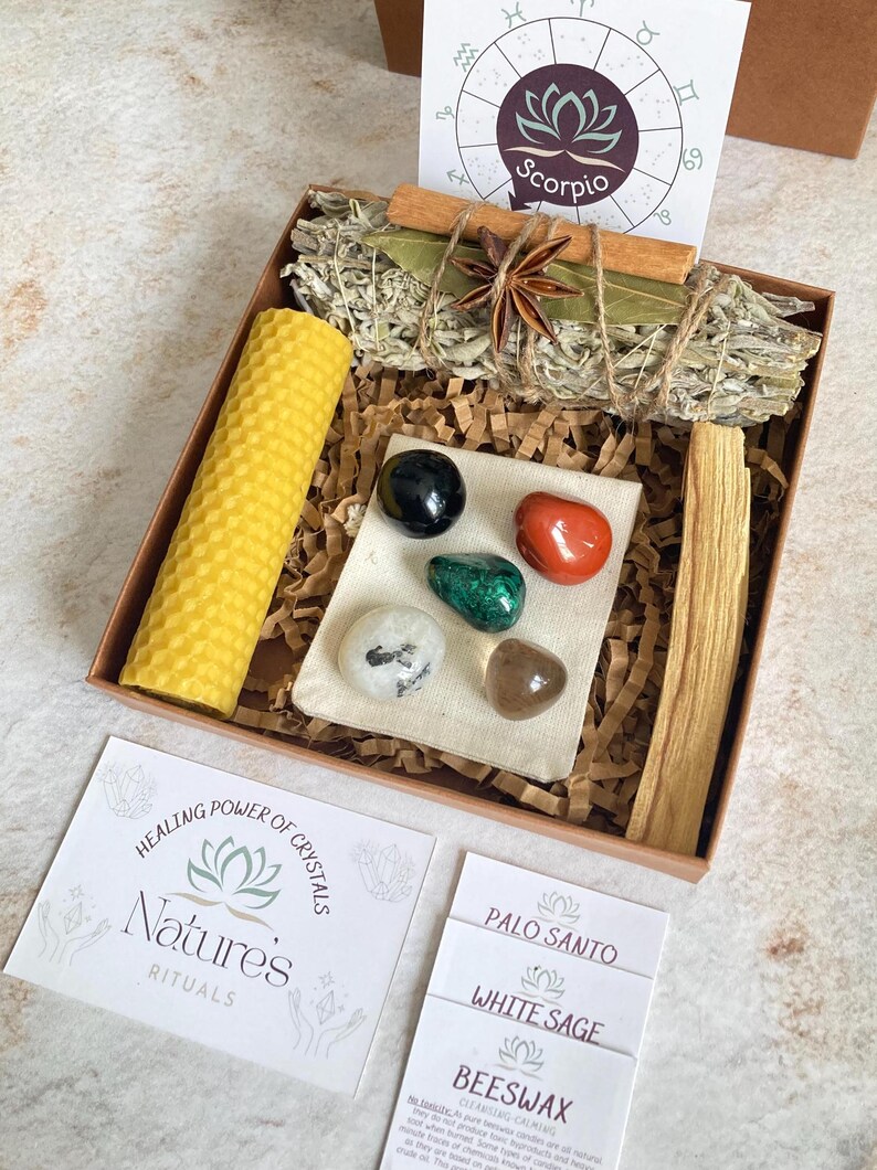 May include: A wooden box filled with items for a spiritual ritual. The box contains a white sage smudge stick, palo santo stick, beeswax candle, and a small pouch with crystals. The box also includes a card with the text "Healing Power of Crystals, Nature's Rituals".