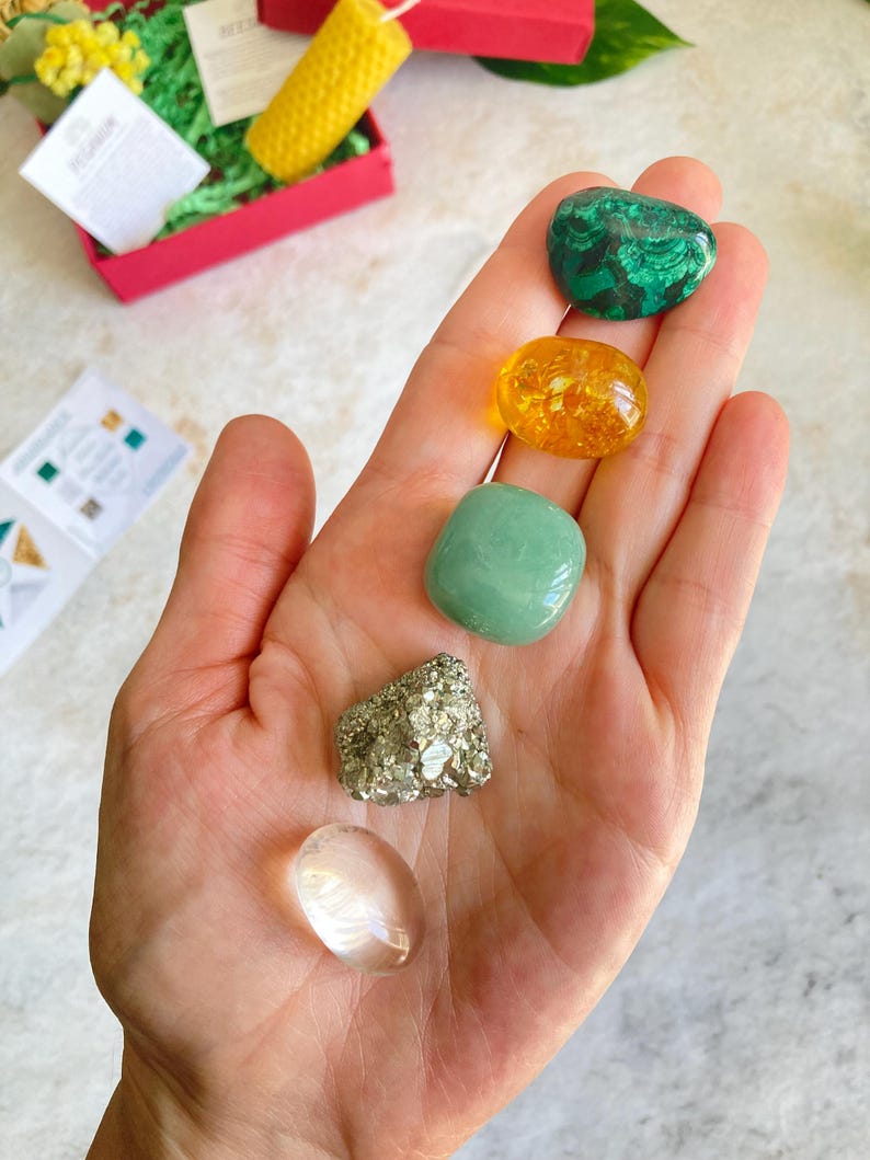 May include: A collection of five tumbled stones, including a clear quartz, a green aventurine, a green malachite, a gold pyrite, and a yellow citrine.
