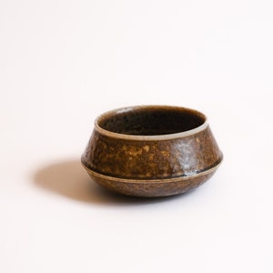 May include: A small, brown ceramic bowl with a white rim. The bowl has a textured surface and a slightly flared lip.