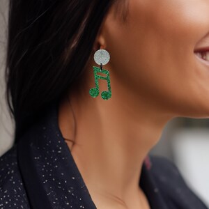 May include: A pair of earrings with a silver glitter disc and a green glitter music note design. These earrings are a playful accessory, ideal for music enthusiasts. A unique and stylish addition to any jewellery collection.