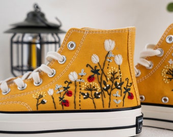Puede incluir: Un par de zapatillas de lona amarillas de caña alta con diseños florales bordados y un logotipo Converse All Star negro.