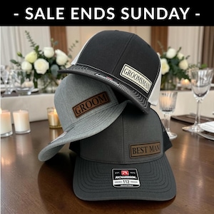 May include: Three adjustable trucker hats stacked together. The top hat is black and white with a patch reading GROOMSMAN. The middle hat is heather gray with a brown patch reading GROOM. The bottom hat is dark gray with a brown patch reading BEST MAN.
