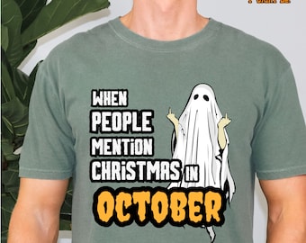 Peut inclure: Un t-shirt vert avec un fantôme blanc faisant la grimace et montrant le doigt d'honneur. Le texte sur le t-shirt est "When people mention Christmas in October".