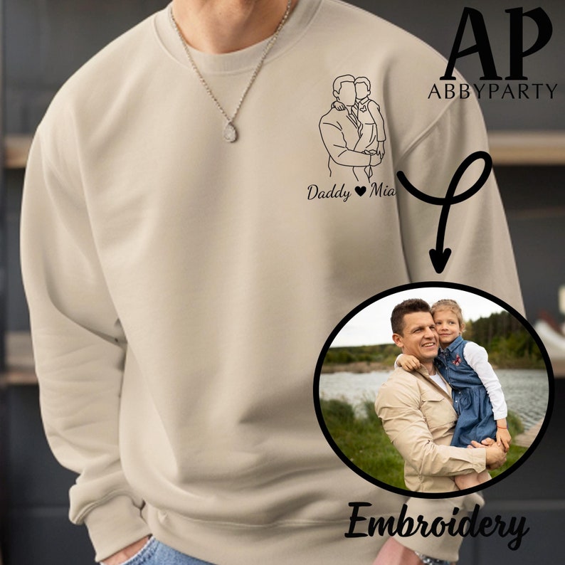 May include: A beige sweatshirt with a black line drawing of a father and daughter with the text "Daddy Mia" underneath. The sweatshirt is shown with an embroidered image of a father and daughter in a circle with the word "Embroidery" underneath.
