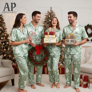 May include: Four people wearing matching green Christmas pyjamas with a white tree and bear pattern. The pyjamas have black trim. They are holding gifts, candy canes, and a wreath in front of a Christmas tree.