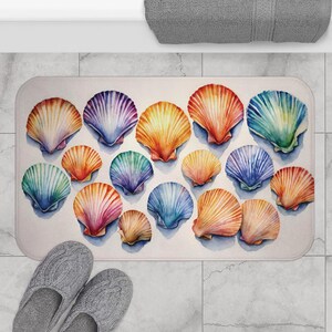 May include: A bath mat with a watercolor design of colorful seashells. The shells are arranged in a random pattern and are painted in shades of blue, green, purple, orange, and yellow.