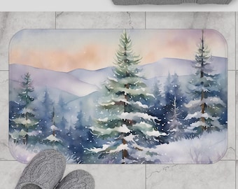 May include: A rectangular bath mat featuring a watercolor painting of a snowy forest scene. The design includes snow-covered evergreen trees, mountains, and a soft, pastel-colored sky. The mat is placed on a tiled floor, with a pair of gray slippers visible.
