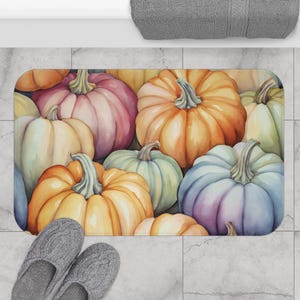 Könnte beinhalten: Ein rechteckiger Badteppich mit einem Aquarelldesign aus Kürbissen in Orange, Rosa, Grün und Blau. Die Kürbisse haben grüne Stiele. Graue Hausschuhe befinden sich unten links.