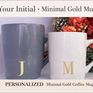 Pode incluir: Duas canecas de cerâmica, uma cinza e outra branca, cada uma com uma inicial dourada. A caneca cinza tem um "J" dourado, e a caneca branca tem um "M" dourado. As canecas são rotuladas como "Your Initial • Minimal Gold Mug" e "PERSONALIZED Minimal Gold Coffee Mug".
