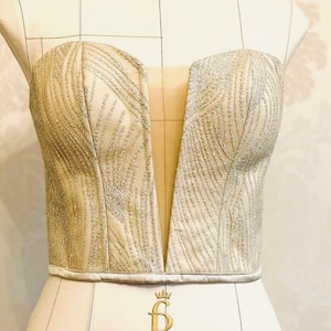 Pode incluir: Um corpete sem alças, de lantejoulas prateadas, com um decote em V profundo. O corpete está em um manequim branco com o texto "Royal Dress forms Italy design" na parte inferior.