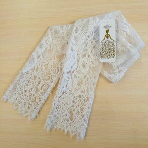 Peut inclure: Gants de mari&eacute;e en dentelle blanche avec des embellissements de perles. Les gants sont pli&eacute;s en deux et portent une petite &eacute;tiquette blanche avec le texte "Anastasia Bridal".