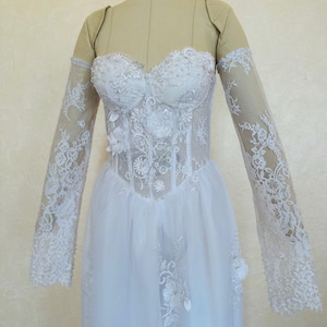 Peut inclure: Une robe de mari&eacute;e en dentelle blanche avec un corsage ajust&eacute; et une jupe ample. La robe a des manches longues avec des d&eacute;tails en dentelle et un d&eacute;collet&eacute; en c&oelig;ur.