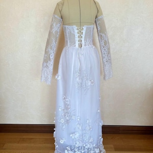 Peut inclure: Robe de mari&eacute;e blanche en dentelle &agrave; manches longues et dos lac&eacute;. La robe a une jupe ample et est d&eacute;cor&eacute;e d'applications florales.