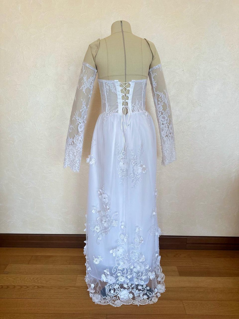 Peut inclure: Robe de mari&eacute;e blanche en dentelle &agrave; manches longues et dos lac&eacute;. La robe a une jupe ample et est d&eacute;cor&eacute;e d'applications florales.