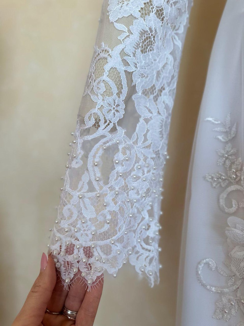 Peut inclure: Tissu de dentelle blanche avec des embellissements de perles. La dentelle a un motif floral et les perles sont cousues autour des bords.