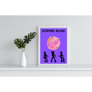 Puede incluir: Una impresión enmarcada con un fondo morado y el texto "STAYIN' ALIVE" en negro. Una bola de discoteca rosa cuelga sobre tres siluetas negras de personas bailando.