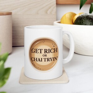 May include: White ceramic mug with a brown coffee cup design and the text "Get Rich or Chai Tryin'" printed on it.