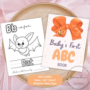 Op de afbeelding: Twee kinderboeken op een houten dienblad. Eén boek bevat een vleermuisillustratie met het woord "Bat" en "Bb is for". Het andere boek zegt "Baby's First ABC BOOK" met een oranje strikillustratie. De afbeelding bevat de tekst "INCLUDED Sizes - 5x7 8.5x11 BONUS Table Sign".