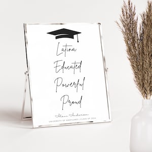 May include: A white framed sign with a black graduation cap silhouette at the top. The words "Latina, Educated, Powerful, Proud" are written in black cursive script. Below the words is the name "Alani Anderson" and the text "University of Maryland | Class of 2024".