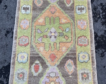 May include: A vintage green and brown rug with a geometric pattern. The rug has a central medallion with a floral design and a border with repeating motifs.