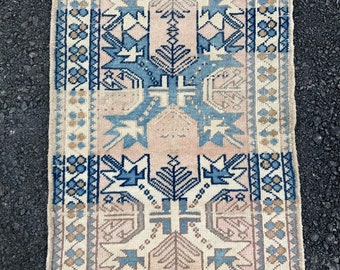May include: A vintage Turkish rug with a geometric pattern in shades of blue, pink, and beige. The rug has a fringed edge and is made of wool.