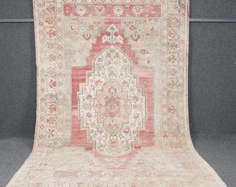 May include: A vintage Turkish rug with a cream background and a large, intricate red and cream floral design in the centre. The rug has a faded, distressed look and is bordered by a repeating pattern of small floral motifs.