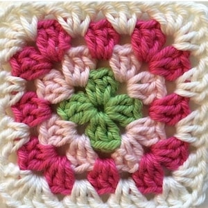 May include: A crocheted square with a green center surrounded by pink and white flowers.