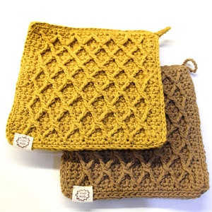 Può includere: Due presine all'uncinetto, una di colore giallo senape con un motivo a rombi e l'altra di colore marrone con un motivo a treccia. Entrambe le presine hanno un piccolo cartellino con la scritta "Hand Made".