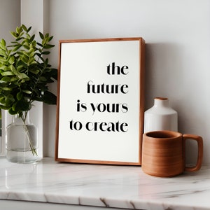 Könnte beinhalten: Ein gerahmter Druck mit dem Text "the future is yours to create" in schwarzer Schrift auf weißem Hintergrund. Der Druck liegt auf einer weißen Marmor-Arbeitsplatte mit einer weißen Keramikvase und einer braunen Keramiktasse.