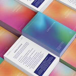 May include: Stacks of cards with a gradient design in shades of pink, orange, and blue. The cards have text in German, including "LOSLASSEN" and "LICHT & SCHATTEN". The design features a minimalist logo.