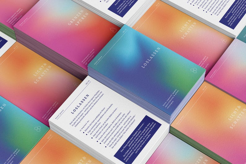 May include: Stacks of cards with a gradient design in shades of pink, orange, and blue. The cards have text in German, including "LOSLASSEN" and "LICHT & SCHATTEN". The design features a minimalist logo.