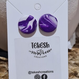 May include: A pair of purple and white marbled stud earrings. The earrings are displayed on a white card with the text "Tekesh Creations" and social media handles.