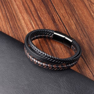 May include: A black and brown leather bracelet with a braided design and a magnetic clasp.