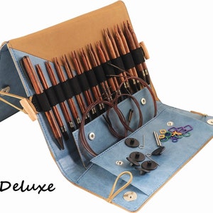Peut inclure: Un étui en cuir bleu et marron contenant un jeu d'aiguilles à tricoter en bois, des aiguilles à câble, des marqueurs de mailles et un enfile-aiguille. L'étui porte l'inscription "Deluxe" sur le devant.