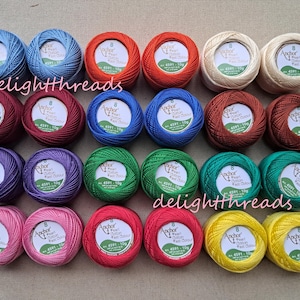 May include: A collection of colorful Anchor Pearl Cotton thread balls in various shades, including blue, red, green, and yellow. Each ball is labeled with product information. The word "delightthreads" is visible.