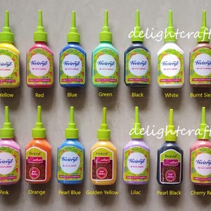以下が含まれることがあります： 黄色、赤、青、緑、黒、白、バーントシェンナなど、さまざまな色のFevicryl 3Dアウトライナーのコレクション。ボトルには緑色のノズルが付いており、ブランド名と製品の詳細が記載されています。「delightcrafts」というテキストも表示されています。