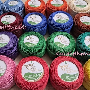 May include: A collection of colorful Anchor Pearl Cotton thread balls in various shades, including blue, green, red, and yellow. Each ball is labeled with the brand name and product information. The image is well-lit, showcasing the vibrant colors of the thread.