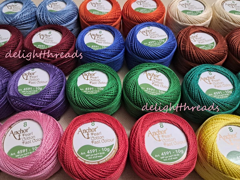 May include: A collection of colorful Anchor Pearl Cotton thread balls in various shades, including blue, green, red, and yellow. Each ball is labeled with the brand name and product information. The image is well-lit, showcasing the vibrant colors of the thread.
