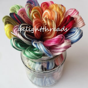 May include: A clear glass jar filled with colorful embroidery floss. The floss is arranged in a bouquet of various colors, including pink, orange, blue, green, and yellow. The text "delighththreads" is visible on the jar.