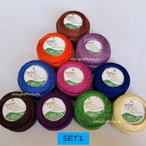 May include: A collection of ten colorful balls of Anchor Pearl Cotton thread, each with a label indicating the product details. The thread colors include brown, orange, purple, pink, blue, green, and cream. The text "SET1" is visible at the bottom.