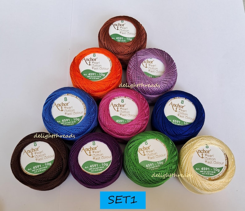 May include: A collection of ten colorful balls of Anchor Pearl Cotton thread, each with a label indicating the product details. The thread colors include brown, orange, purple, pink, blue, green, and cream. The text "SET1" is visible at the bottom.