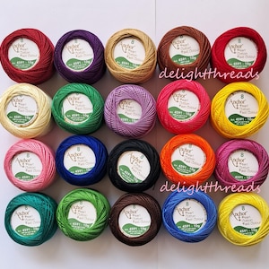Puede incluir: Una variedad de ovillos de hilo Anchor Pearl Cotton de colores vibrantes, incluyendo rojo, morado y verde. Cada ovillo est&aacute; etiquetado con el nombre de la marca y detalles del producto. La imagen est&aacute; bien iluminada, mostrando los colores vivos del hilo.