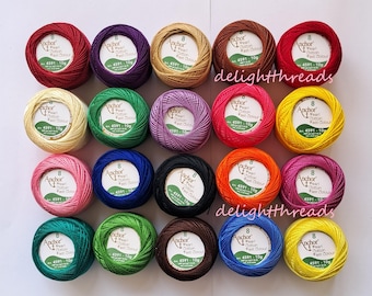 May include: An assortment of colorful Anchor Pearl Cotton thread balls in various shades, including red, purple, gold, and green. Each ball is labeled with the brand name and product details. The image is well-lit, showcasing the vibrant colors of the thread.