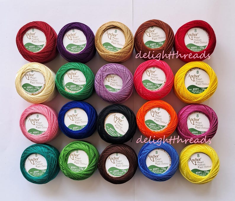 Puede incluir: Una variedad de ovillos de hilo Anchor Pearl Cotton de colores vibrantes, incluyendo rojo, morado y verde. Cada ovillo est&aacute; etiquetado con el nombre de la marca y detalles del producto. La imagen est&aacute; bien iluminada, mostrando los colores vivos del hilo.