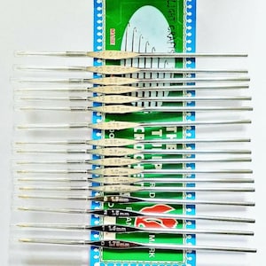 Peut inclure: Un ensemble de crochets argentés de différentes tailles, présentés sur une carte bleue et verte. Les tailles, allant de 0,4 mm à 1,75 mm, sont indiquées. La carte porte l'inscription "DELIGHT CRAFTS".