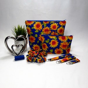 Gift set in royal blue and yellow with a large sunflowers printed on the fabric. The set comprises of a make up bag with royal blue zip, Larger wash bag with royal blue zip, 3 sizes of keyrings, small, medium and large. Two hair scrunchies.