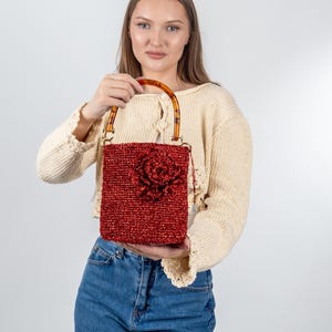 Peut inclure: Un sac à main en crochet rouge avec un grand détail de fleur et une poignée en écaille de tortue brune.